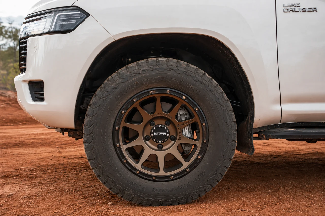 Best Land Cruiser Wheels for a Strong Overland Setup Land Cruiser bronze forged wheel close up with all terrain tire and red dirt background